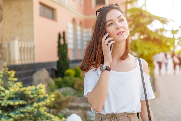 Knappe glimlachende vrouw met mobiele telefoon die op de straat loopt