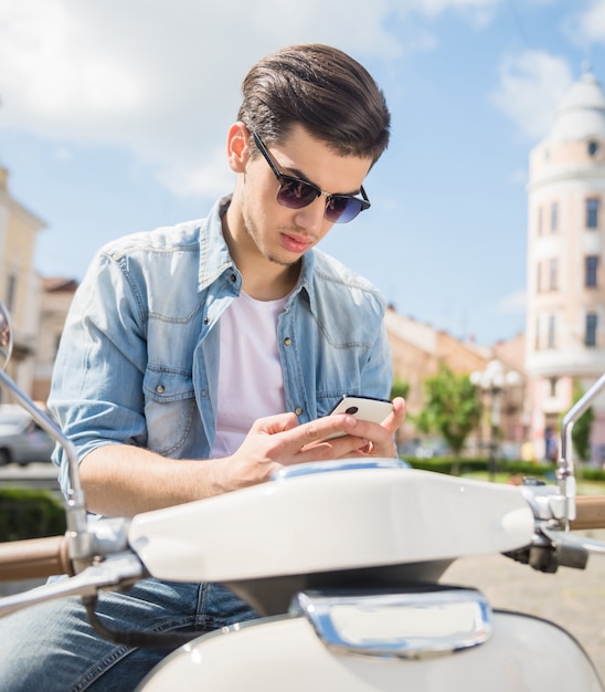 Knappe handige man zittend op een scooter en het gebruik van de telefoon.