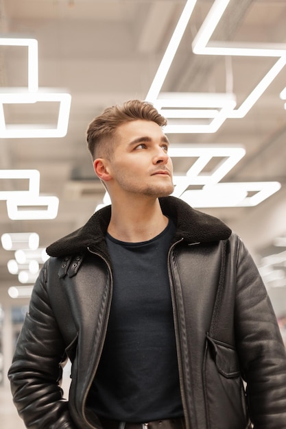 Knappe hipster-manmodel met haar in een modieus zwart leren jack en t-shirt loopt binnenshuis met verlichting