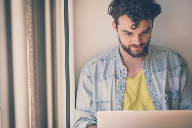 Foto knappe hipster moderne man thuis werken met behulp van laptop