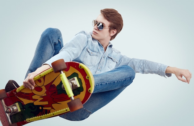 Knappe hipstermens in jeansjasje die de tik op modieus skateboard doen