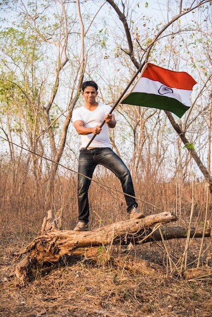 Knappe Indiase jongeman die vasthoudt of zwaait of rent met Indiase driekleurige vlag buiten in de buurt van meer, conceptueel beeld voor de dag van de republiek of de wenskaart van de onafhankelijkheidsdag.