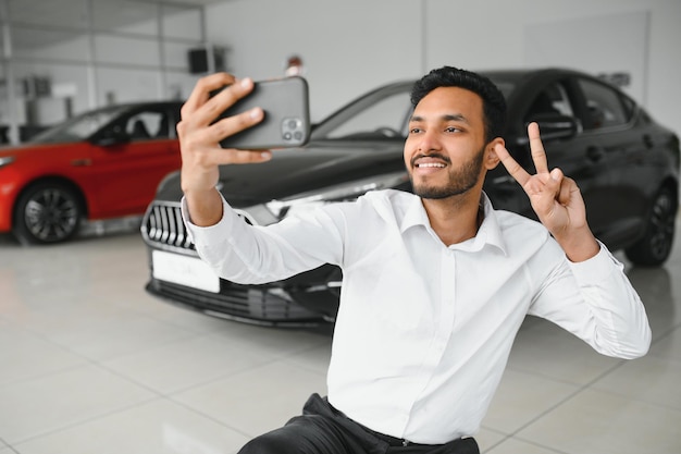 Knappe Indiase man die een selfie met autosleutels maakt naar zijn nieuwe auto in de showroom van de dealer copyspace technologie sociale media delen positiviteit levensstijl reizend toerisme