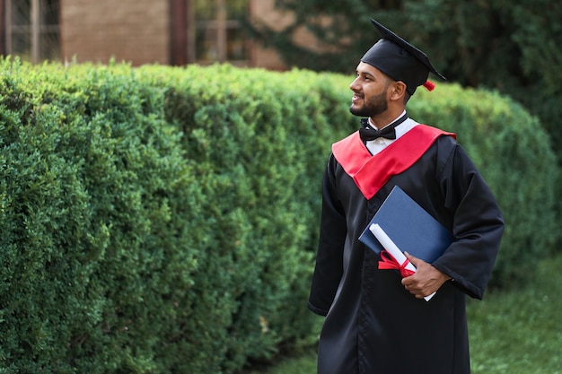 Knappe indiase student die afstuderen op de universiteitscampus viert met diploma in gewaad.