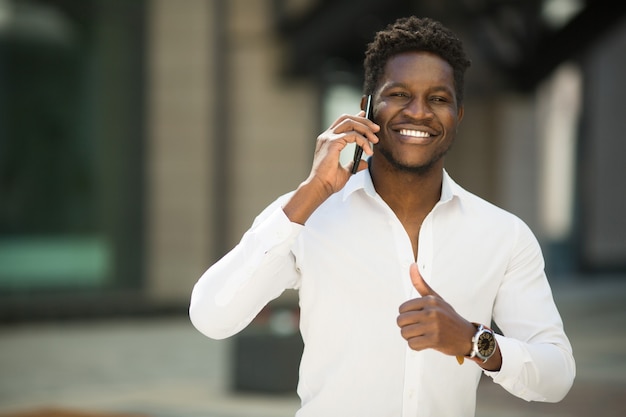 knappe jonge Afrikaanse man in shirt met telefoon met handgebaar