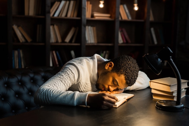 knappe jonge Afrikaanse man slapen op de tafel met boeken