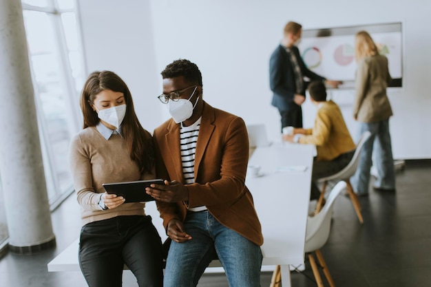 Knappe jonge Afro-Amerikaanse zakenman en schattige zakenvrouw die aan een digitale tablet werkt terwijl ze een gezichtsbeschermend masker draagt