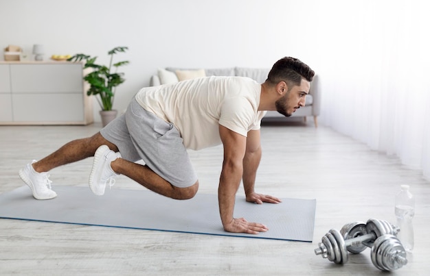 Knappe jonge Arabische man in sportkleding die traint op een yogamat die huishoudelijke fitness doet om zijn