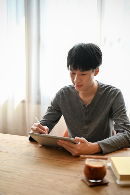 Knappe jonge Aziatische man met behulp van digitale tablet in het café