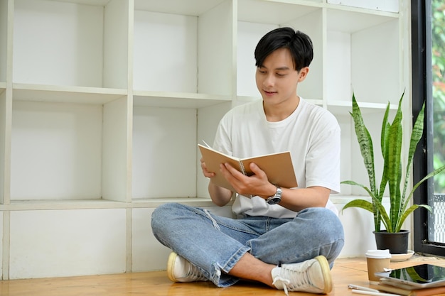 Knappe jonge Aziatische mannelijke student die een boek leest in de campusbibliotheek