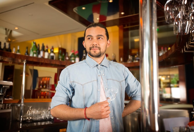 Knappe jonge barman houdt cocktailglas poseren voor de camera. barmedewerker is dom, denkend aan werkroutine. batirsta overweegt nieuw concept voor drankrecepten