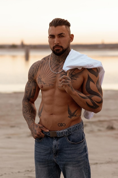 Knappe jonge gespierde Italiaanse man poseren shirtless op het strand zonsondergang zomertijd