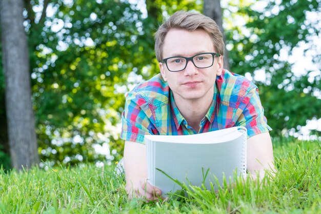 Knappe jonge jongen in kleurrijke shirt lezen terwijl liggend op gras in groen park