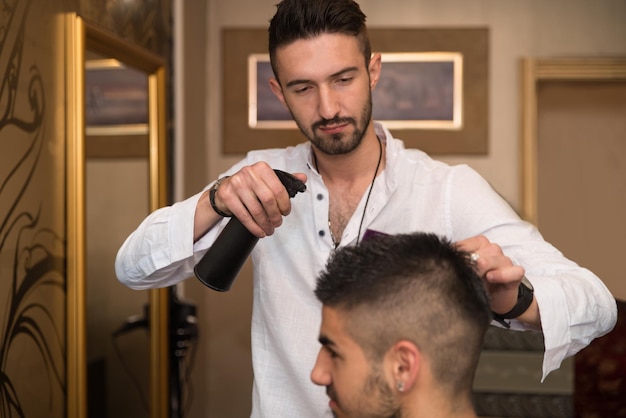 Knappe jonge kapper die een nieuw kapsel geeft aan mannelijke klant in salon