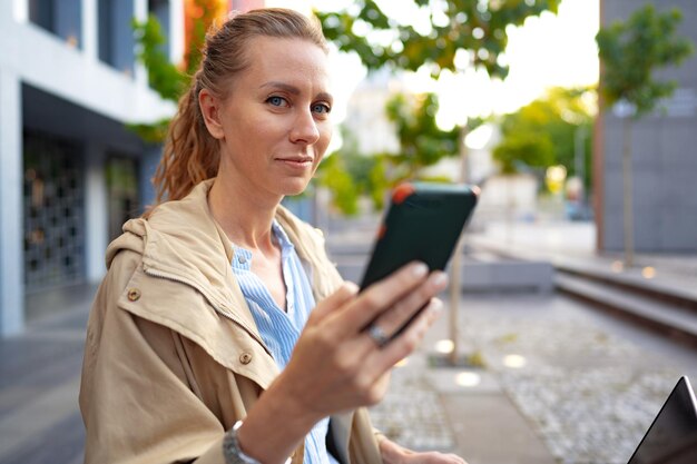 Knappe jonge lachende vrouw met mobiele telefoon die op straat loopt