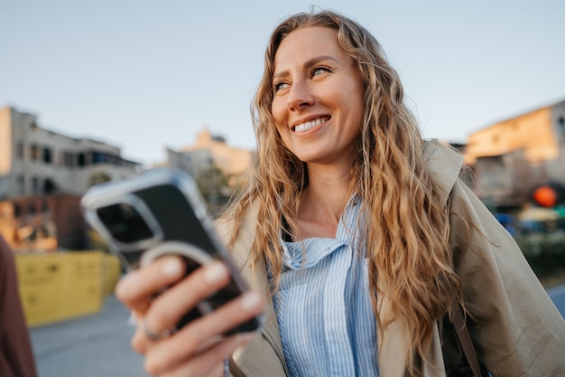 Knappe jonge lachende vrouw met mobiele telefoon die op straat loopt