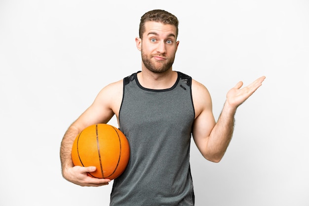 Knappe jonge man die basketbal speelt over een geïsoleerde witte achtergrond die twijfels heeft terwijl hij zijn handen opsteekt