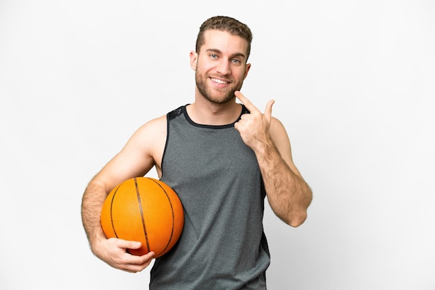 Knappe jonge man die basketbal speelt over een geïsoleerde witte achtergrond en een duim omhoog gebaar geeft