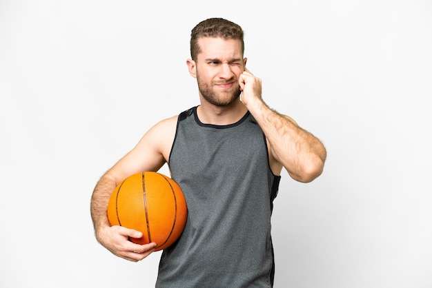 Knappe jonge man die basketbal speelt over een geïsoleerde witte achtergrond, gefrustreerd en oren bedekkend