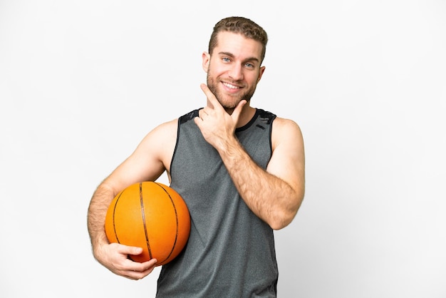 Knappe jonge man die basketbal speelt over een geïsoleerde witte achtergrond, gelukkig en glimlachend