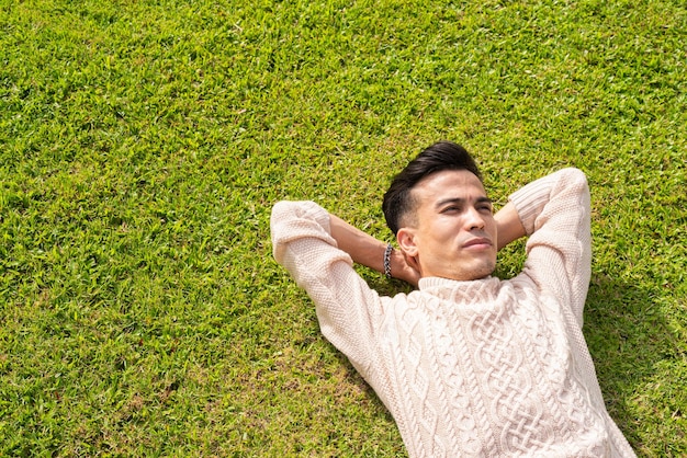 Knappe jonge man die in de zomer in het park op het gras ligt