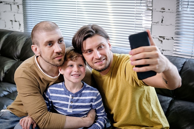 Knappe jonge man die selfie maakt met zijn zoon en echtgenoot wanneer hij thuis op de bank zit