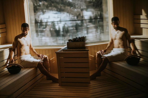 Knappe jonge man die water op hete steen in de sauna giet