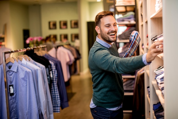 Knappe jonge man het kopen van kleding in de mode winkel