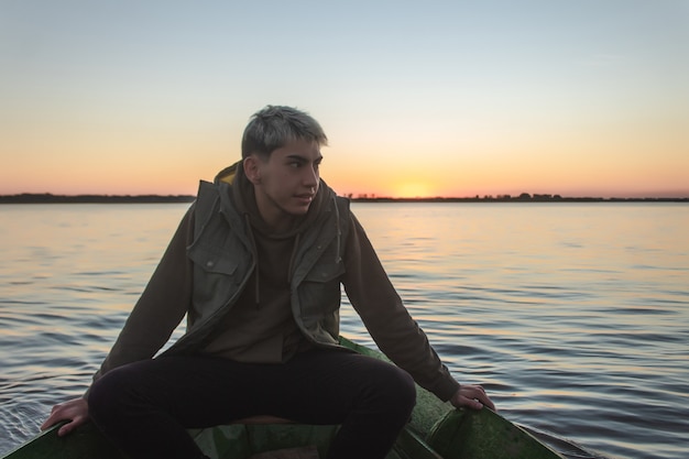 Knappe jonge man in een boot die de zonsondergang op zee waardeert.