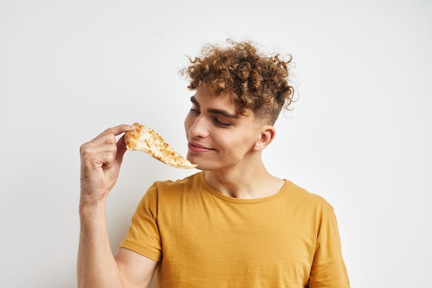 Knappe jonge man in een gele t-shirt die pizza eet Ongewijzigde levensstijl