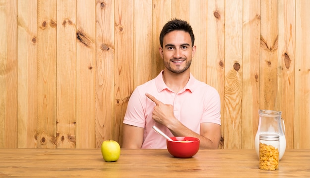 Knappe jonge man in een keuken met ontbijt wijst naar de zijkant om een product te presenteren