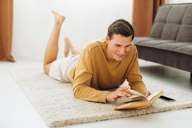 Knappe jonge man in gele vrijetijdskleding die thuis een boek leest
