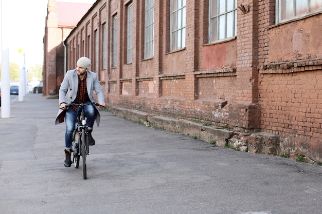 Knappe jonge man in grijze jas en hoed op een fietsstraat in de stad.
