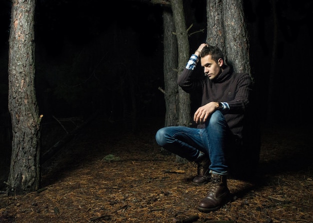 Knappe jonge man in het bos een man in warm licht poseert 's nachts in het bos