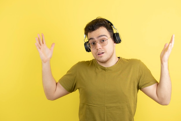 Knappe jonge man in koptelefoon permanent over gele muur.