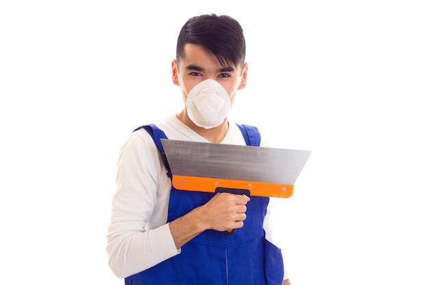 Knappe jonge man in shirt en blauwe overall met wit gasmasker op zijn gezicht met spatel