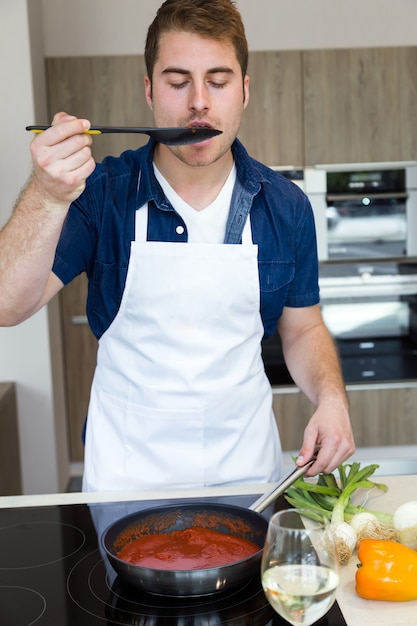 Foto knappe jonge man koken tomaten saus in de keuken thuis.