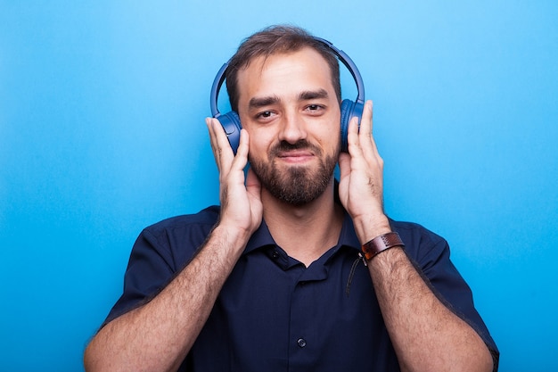 Knappe jonge man luisteren naar muziek via koptelefoon op blauwe achtergrond