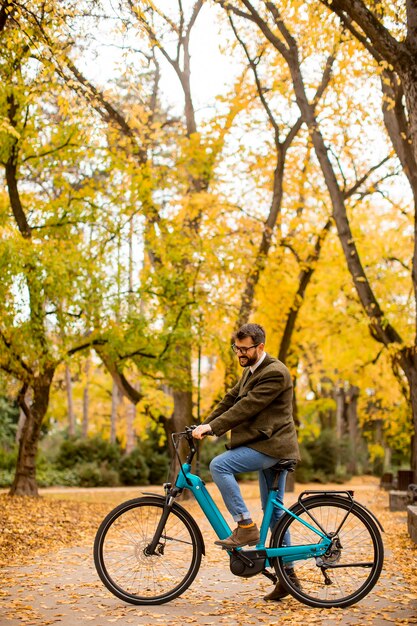 Knappe jonge man met elektrische fiets in het herfstpark