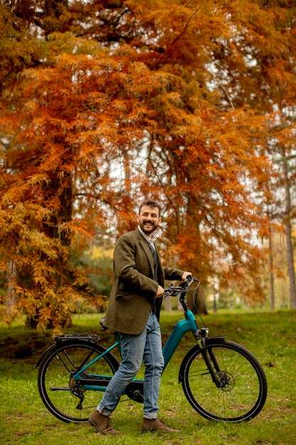 Knappe jonge man met elektrische fiets in het herfstpark
