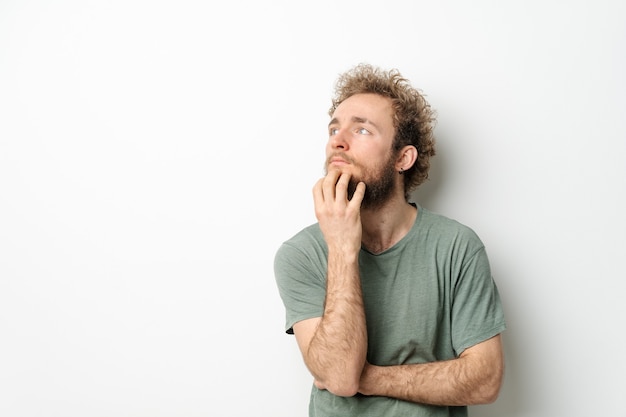 Knappe jonge man met krullend haar in olijf t-shirt opzoeken weg geïsoleerd op witte muur