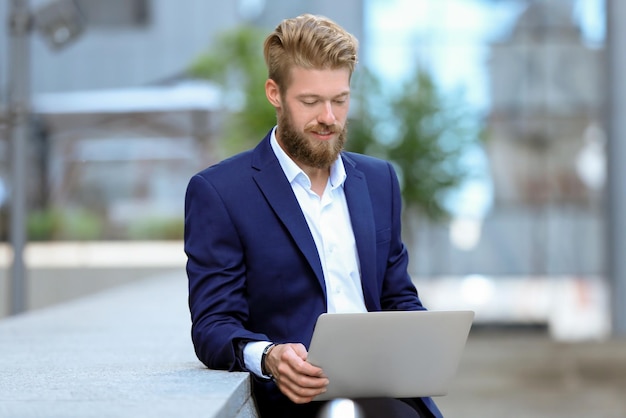 Knappe jonge man met laptop buitenshuis