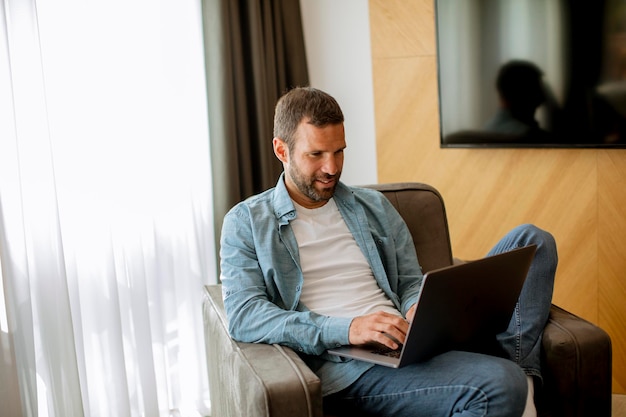 Knappe jonge man met laptopcomputer in de woonkamer