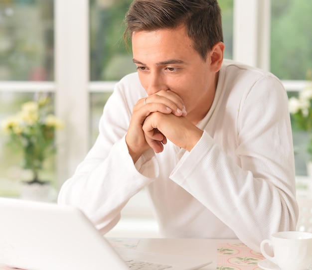 Knappe jonge man met laptopcomputer thuis