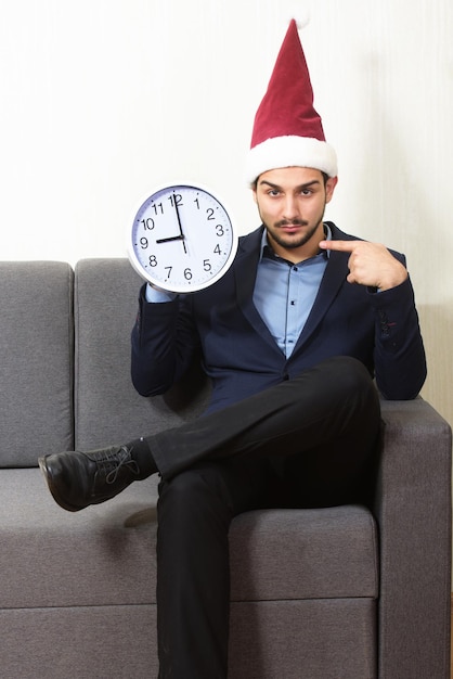 Foto knappe jonge man met rode kerstmuts wijzend op de klok