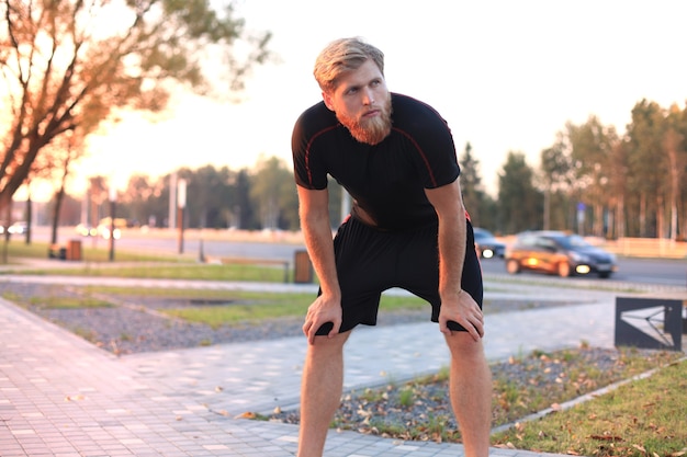 Knappe jonge man na het hardlopen uitrusten na joggen in het park bij zonsondergang of zonsopgang