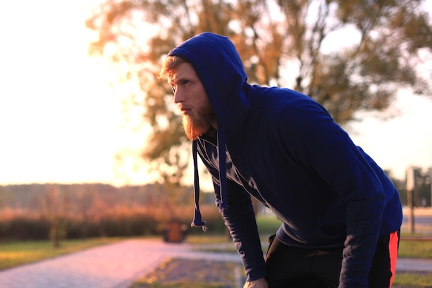 Knappe jonge man na het hardlopen uitrusten na joggen in het park bij zonsondergang of zonsopgang