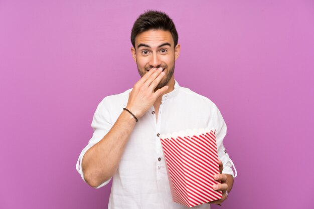 Knappe jonge man over paarse muur houden popcorns