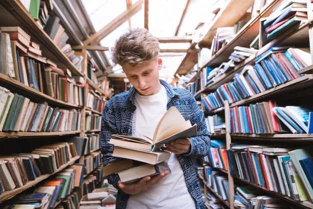 Knappe jonge man staat in een oude openbare bibliotheek met boeken in zijn handen en leest.