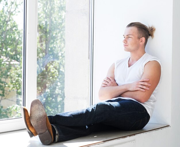 Knappe jonge man zittend op de vensterbank, levensstijl concept